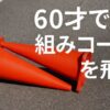 アスファルトの上に倒れて重なった2つの赤いコーン。右上には『60才でも組みコーンを飛ぶ』という白いテキストが表示されている。