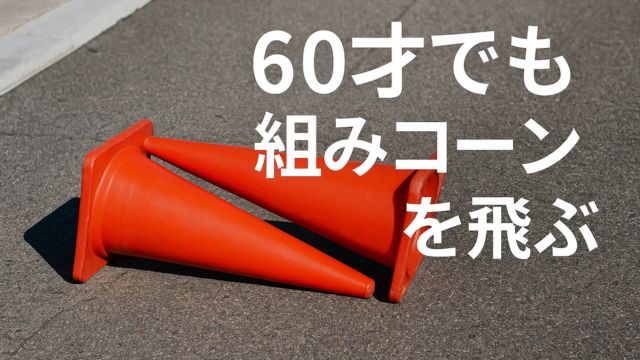 アスファルトの上に倒れて重なった2つの赤いコーン。右上には『60才でも組みコーンを飛ぶ』という白いテキストが表示されている。